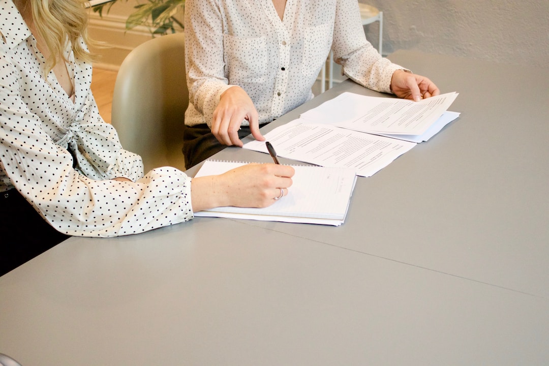Two women sit at a table discussing paperwork